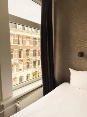 a bedroom with a bed and a window with a building at Hotel Vondel Garden in Amsterdam