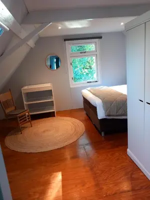 a bedroom with a bed and a chair and a window at Uniek vakantiehuis - nabij molen, meer, strand & stad' in Hoorn
