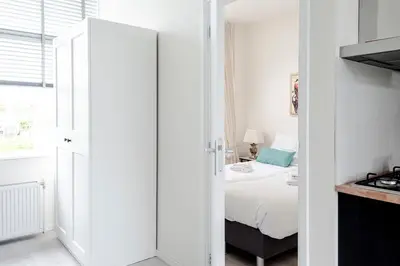 a white bedroom with a bed and a kitchen at Sea Shell apartment in Zandvoort