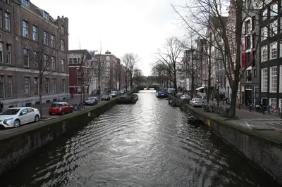 a river in a city with cars parked on the sides at Amsterdam Downtown Hotel Canal View in Amsterdam