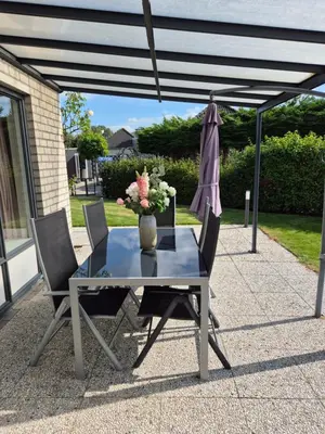a table and chairs with a vase of flowers and an umbrella at Nordseeperle Dirkshorn Nordholland, mit Klimaanlage und Sauna in Dirkshorn
