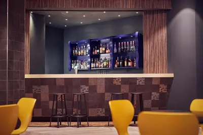 a bar with yellow bar stools and bottles of alcohol at Inntel Hotels Amsterdam Centre in Amsterdam