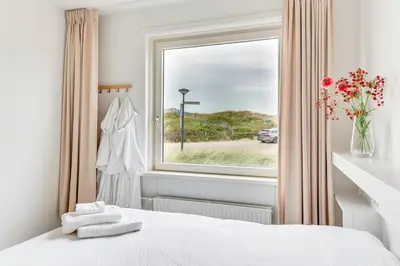 a bedroom with a window and a white bed with towels at Vernieuwd Zeezicht Villa Strand Luxe in Bergen aan Zee
