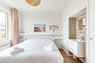 a white bedroom with a white bed and a window at Vernieuwd Zeezicht Villa Strand Luxe in Bergen aan Zee