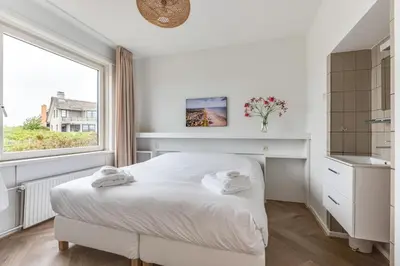 a white bedroom with a bed and a window at Vernieuwd Zeezicht Villa Strand Luxe in Bergen aan Zee