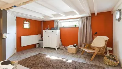 a living room with orange walls and a chair at Benedenverdieping in Woonboot met tuinterras in Utrecht
