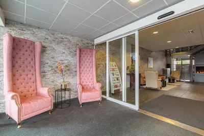 two pink chairs in a room with a brick wall at Leonardo Hotel Lelystad City Center in Lelystad