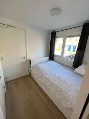 a small bedroom with a bed and a window at Duinroos aan Zee in Egmond aan Zee