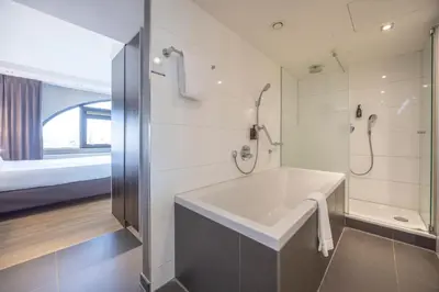 a bathroom with a tub and a shower and a bed at Fletcher Hotel-Restaurant Nieuwegein-Utrecht in Nieuwegein