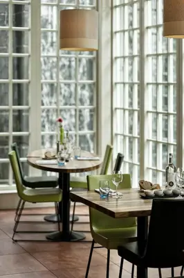 a dining room with two tables and chairs and windows at Inntel Hotels Amsterdam Zaandam in Zaandam