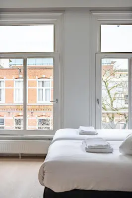 a white bedroom with two beds and two windows at Hotel Kap City Centre in Amsterdam