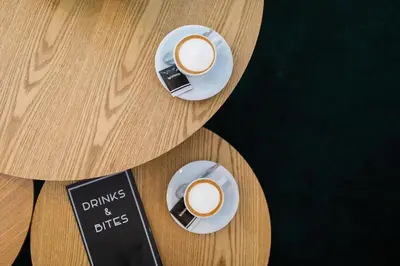 two cups of coffee on plates on a wooden table at Gooiland Hotel in Hilversum