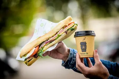 a person holding a sandwich and a cup of coffee at Campanile Hotel & Restaurant Gouda in Gouda
