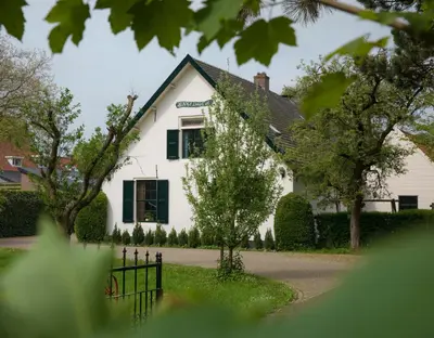 a white house with green windows and a gate at De Dinkelhoeve in Heemstede
