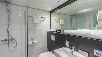 a bathroom with a shower and a sink and a mirror at Postillion Amersfoort Veluwemeer in Putten