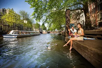 two people sitting on a ledge next to a canal at Mister Highland Hotel in Amsterdam