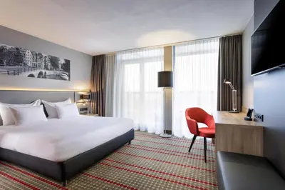 a hotel room with a bed and a desk and a television at Ramada by Wyndham Amsterdam Airport Schiphol in Badhoevedorp