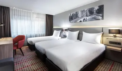 a hotel room with two beds and a desk at Ramada by Wyndham Amsterdam Airport Schiphol in Badhoevedorp