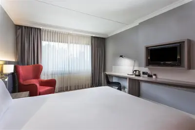 a hotel room with a bed and a chair and a television at Ramada by Wyndham Amsterdam Airport Schiphol in Badhoevedorp