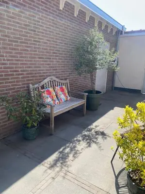 a wooden bench with two pillows sitting next to a brick wall at Guesthouse Katwijk aan Zee in Katwijk aan Zee