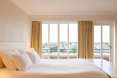 a bedroom with a white bed and a large window at Van der Valk Palace Hotel Noordwijk in Noordwijk aan Zee