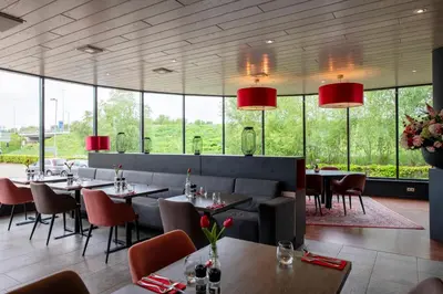 a restaurant with tables and chairs and large windows at Bastion Hotel Almere in Almere
