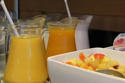 two glasses of orange juice and a bowl of fruit at Bastion Hotel Amsterdam Zuidwest in Amsterdam