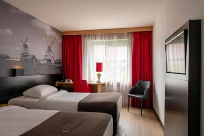 a hotel room with two beds and a window with red curtains at Bastion Hotel Zaandam in Zaandam
