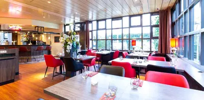 a restaurant with tables and red chairs and windows at Bastion Hotel Bussum Hilversum in Bussum