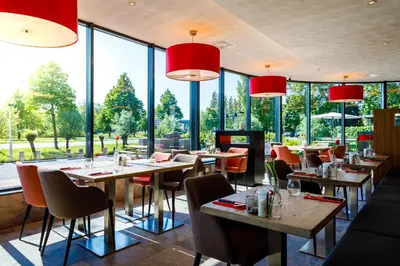 a restaurant with tables and chairs and large windows at Bastion Hotel Haarlem Velsen in Santpoort-Noord