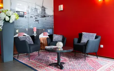 a waiting room with chairs and a table and a red wall at Bastion Hotel Leiden Oegstgeest in Oegstgeest