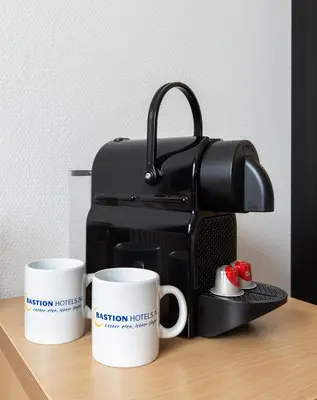 two coffee cups sitting on a table with a coffee maker at Bastion Hotel Leiden Voorschoten in Leiden
