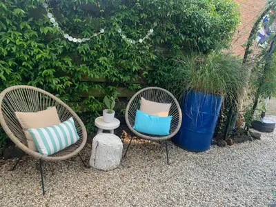 two wicker chairs with pillows sitting next to a hedge at Meerpaal 43 Bergen in Bergen