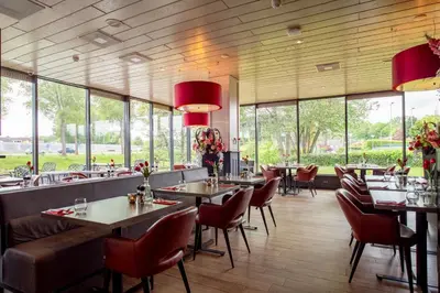 a restaurant with tables and chairs and large windows at Bastion Hotel Schiphol Hoofddorp in Hoofddorp