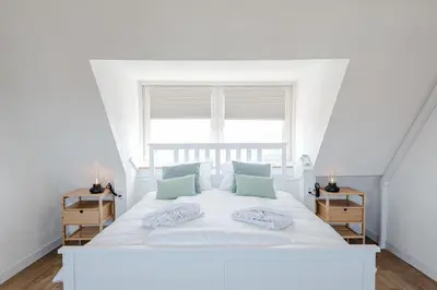a white bedroom with a white bed and a window at Albatros aan Zee - Studio in Zandvoort