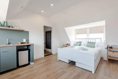 a white bedroom with a white bed and a fireplace at Albatros aan Zee - Studio in Zandvoort