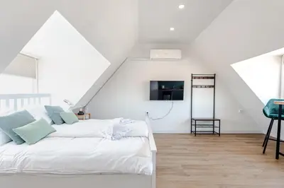 a white bedroom with a bed and a tv at Albatros aan Zee - Studio in Zandvoort