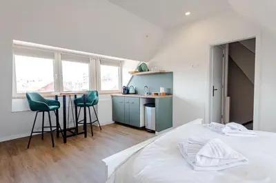 a bedroom with a bed and a kitchen with stools at Albatros aan Zee - Studio in Zandvoort