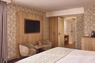 a hotel room with a bed and two chairs and a television at Van der Valk Hotel Leusden - Amersfoort in Leusden