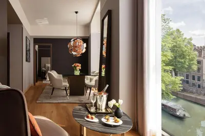 a living room with a table and a large window at Anantara Grand Hotel Krasnapolsky Amsterdam in Amsterdam