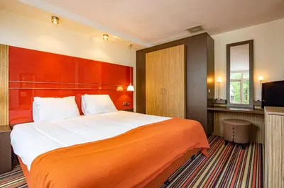 a hotel room with a large bed with an orange blanket at Fletcher Hotel Restaurant Amersfoort in Amersfoort