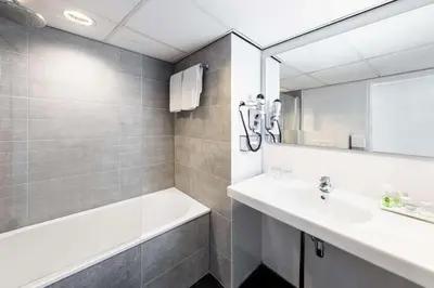 a bathroom with a sink and a tub and a mirror at NH Amsterdam Caransa in Amsterdam