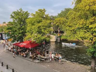 a group of people sitting at a restaurant next to a river at Canal View Stay Amsterdam in Amsterdam