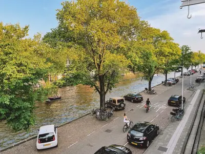 a street with cars parked next to a river at Canal View Stay Amsterdam in Amsterdam