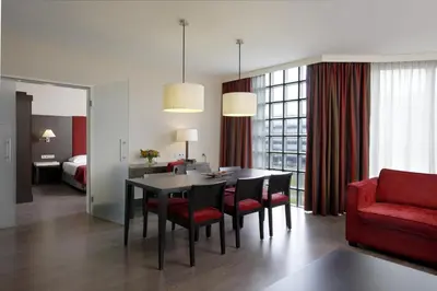 a living room with a dining room table and a red couch at NH Amsterdam Schiphol Airport in Hoofddorp