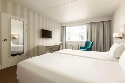 a hotel room with a large white bed and a chair at NH Amsterdam Schiphol Airport in Hoofddorp