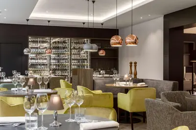 a restaurant with yellow chairs and tables and a bar at NH Bussum Jan Tabak in Bussum