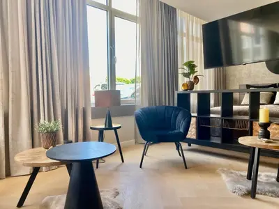 a living room with a blue chair and tables at Glücklich am Meer Suite Deluxe mit Wellnesszugang in Egmond aan Zee