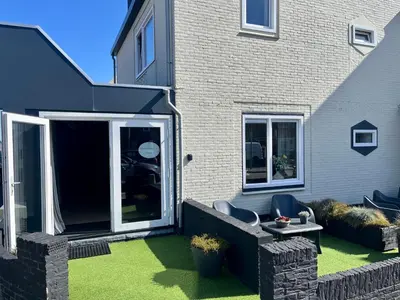 a backyard with a lawn with chairs and a house at Glücklich am Meer Suite Deluxe mit Wellnesszugang in Egmond aan Zee