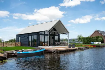 a small cabin on the water with a boat on it at 4 to 6 persons Tulpenacker waterfront in Roelofarendsveen